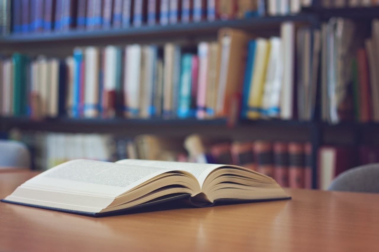 A book on a table with shelves of books in the background.